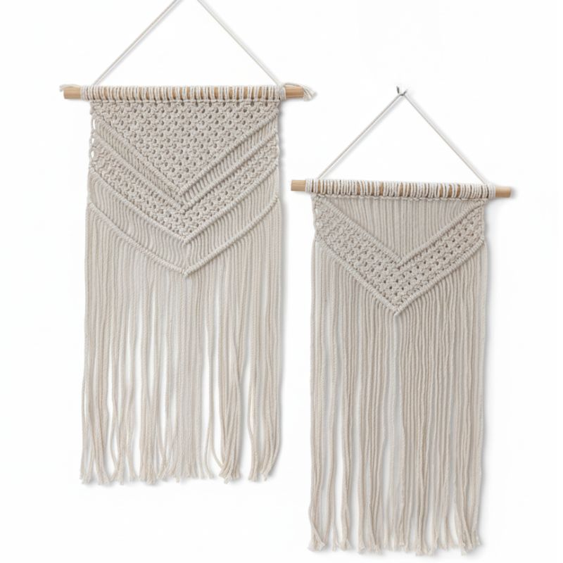 Two cream macrame wall hangings with long fringe and wooden dowel rods for wall decor, one larger and one smaller, featuring chevron patterns.